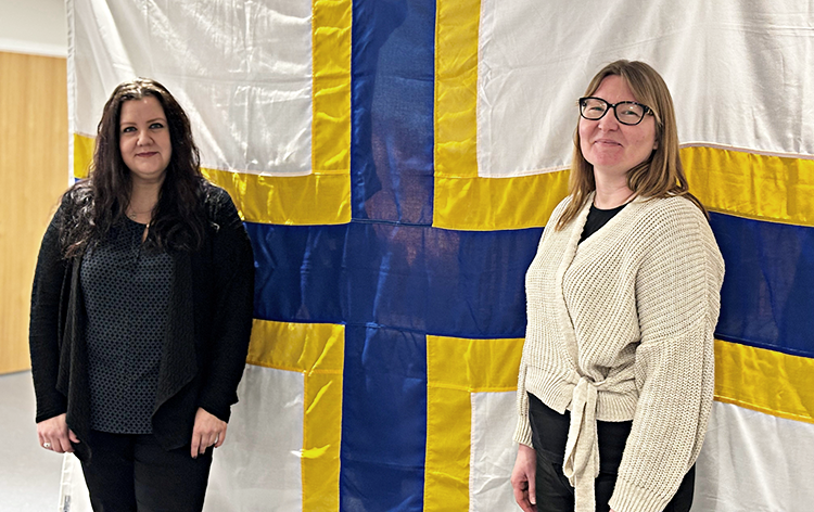 två kvinnor framför sverigefinnarnas flagga