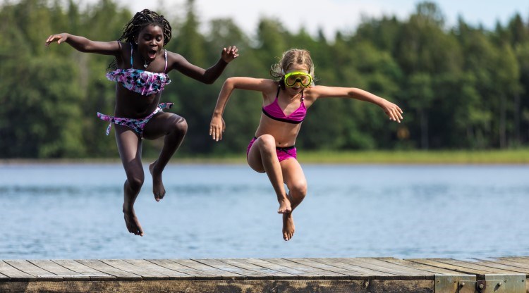 två flickor i luften, de har hoppat från en brygga och landar i vattnet. 