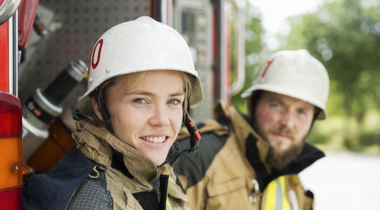 En kvinna och en man i räddningsdräkt poserar vid brandbil.