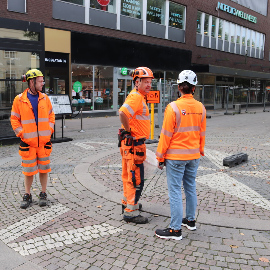 Tre personer i skyddsutrustning står vid byggarbetsplatsen vid Kungsgatan i Trollhättan. Foto.