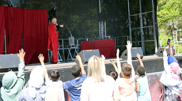 Person på scen pekar ut mot publiken där flera barn står och räcker upp handen.