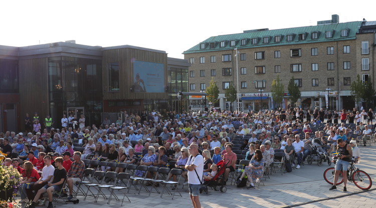 Mängder av människor sitter på stolar på torg utomhus.