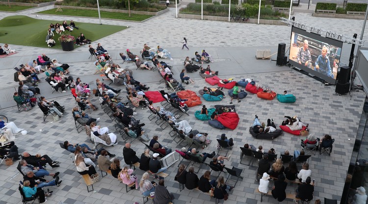 Personer sitter och tittar på utomhusbio på torg